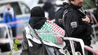 Eine Frau mit Kufiya geht vor der Veranstaltungshalle des Palästina-Kongresses in Berlin an einer Polizeisperre vorbei. (Bild: picture alliance/dpa/Sebastian Gollnow)