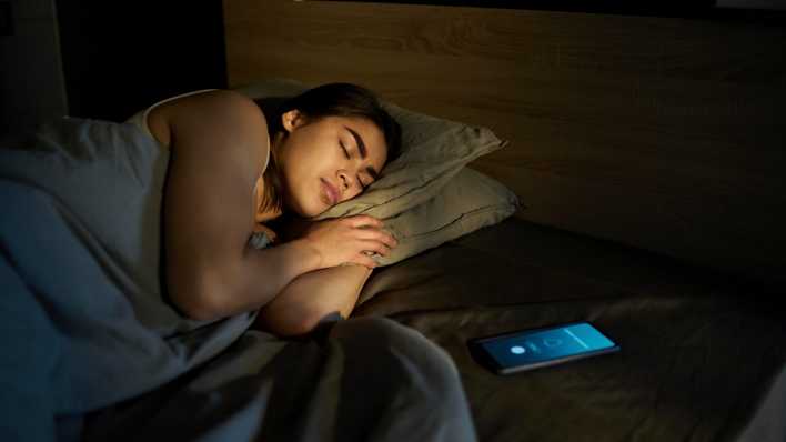 Frau schläft mit Handy beim Bett