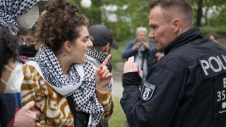 Eine Frau diskutiert während propalästinensischen Demonstration der Gruppe "Student Coalition Berlin" auf dem Theaterhof der Freien Universität Berlin mit einem Polizeibeamten (Bild: Sebastian Christoph Gollnow/dpa)